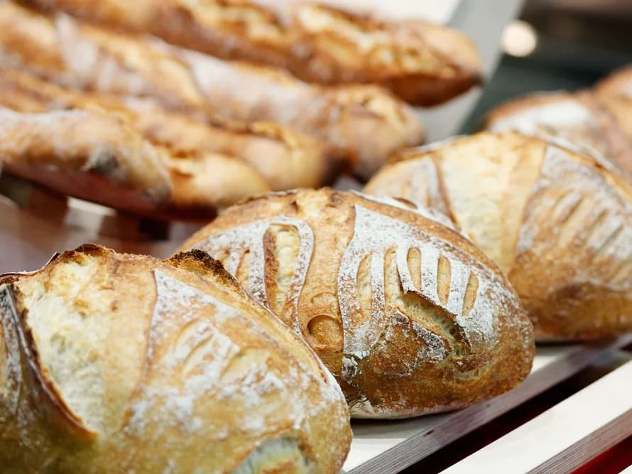 Baguetes e pães rústicos com cortes decorativos, dispostos em bandeja de padaria